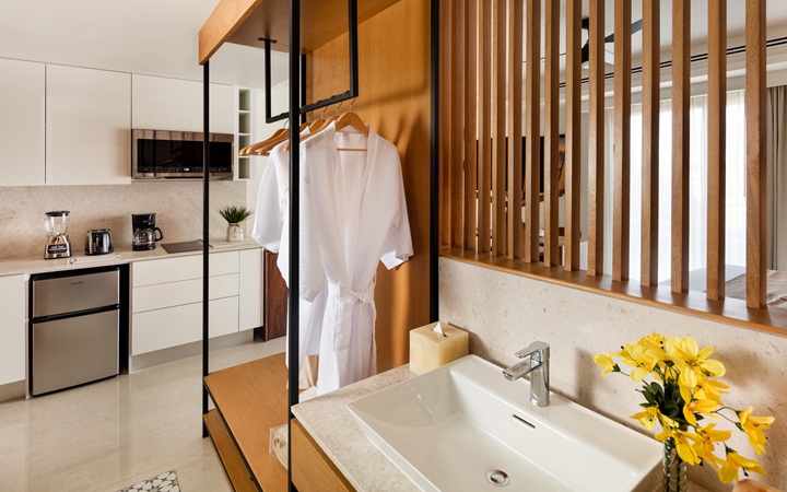 Baño de lujo y área de vestidor que muestra un estilizado tocador con lavabo junto a lujosas batas de baño colgantes y un armario abierto para el almacenamiento de prendas en Kadun Hotel Boutique.