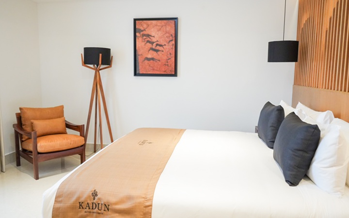 Interior de la suite de lujo que muestra una confortable cama King-size, un cómodo sillón decorativo y un diseño de iluminación sofisticado con una lámpara de techo colgante y una moderna lámpara de piso con pedestal en Kadun Hotel Boutique.